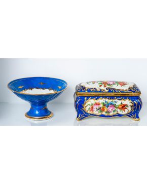 1029-Conjunto en porcelana estilo Sèvres compuesto por frutero y caja rectangular, fondo azul cobalto y flores pintadas.  Altura mayor: 16 cm. 
