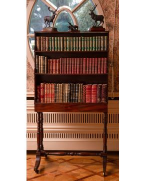 353-Double-sided bookcase o librería Regencia, primer cuarto s. XIX, en madera de caoba con tres niveles y patas unidas por chambrana sobre ruedas. 