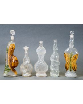 1010-Colección de cinco botellas en vidrio incoloro y esmaltado con representación de caracol y mariposa. Dos de ellas de anís Morel.  Altura mayor: 4