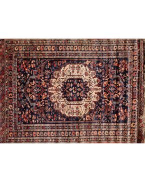 393-Alfombra persa en lana y seda con gran florón central y motivos vegetales en campo y bordura perimetral con elemento